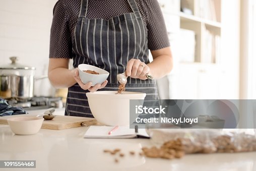 istock Woman in apron adding cocoa powder to the batter in bowl. 1091554468