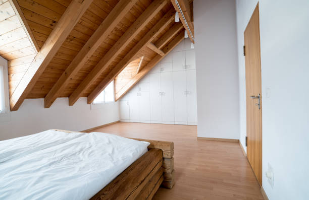 luce intensa moderna camera da letto padronale con pavimenti in parquet in legno e armadio di design e tradizionale letto a travi in legno sotto soffitto inclinato in un appartamento ristrutturato - inhabit foto e immagini stock