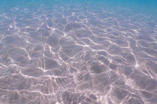 Pristine sandy sea floor and water surface of sunlight and patter