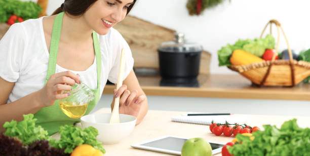 istock Beautiful Hispanic woman cooking in kitchen while using tablet computer and wooden spoon. Housewife found new recipe for dinner or breakfast. Healthy meal and householding concepts 1091631240