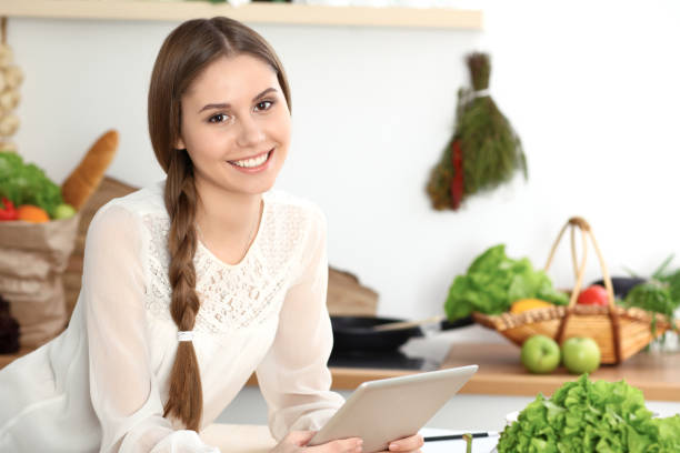 istock Young  woman using tablet while cooking or making online shopping in kitchen. Girl looking at the camera. Healthy lifestyle and vegan meal concepts 1091631320