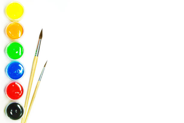 Colorful stationery. Gouache paints of different colors in small plastic jars and wooden paint brushes, empty space for text. Artist set isolated on white background, top view.