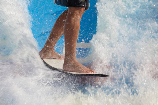 l'uomo si sveglia surf, in sella a una tavola da surf o a una tavola da foot board lungo uno scivolo d'acqua all'aperto allestito - wakeboarding surfing men vacations foto e immagini stock