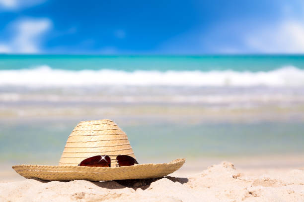 istock Beach accessories on sand for summer vacation concept. Straw hat with sunglasses on white sand against turquoise water amazing ocean and blue sky in the background. 1091652418