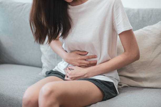 concept de soins de santé vie médicale ou quotidienne : gros ventre de la jeune femme ont une douleur maux d’estomac ou menstruation, assise sur un canapé. - belly ache photos et images de collection