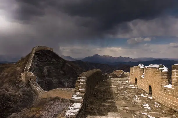 Hiking along the Great Wall of China, moody cloudy backround with fractions of light hitting the wall.