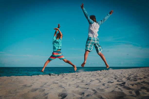 African boy and girl (sister and brother) jumping up on on sandy ocean beach.