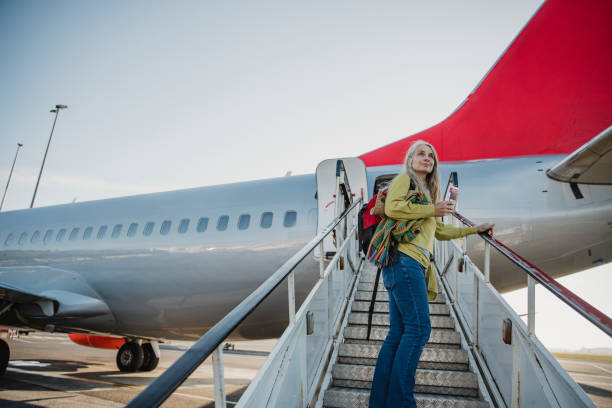 Goodbye Home, Hello World One mature woman is standing on the air-stair of her plane with her boarding pass and has turned round to give one last look to her home before she goes travelling. passenger boarding bridge stock pictures, royalty-free photos & images