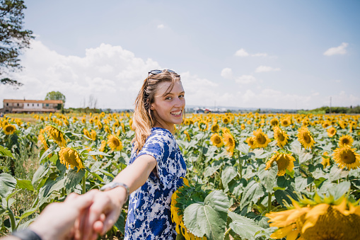 Point of view shot of a young woman grabbing her partners hand to go and explore a sunflower field in Italy.