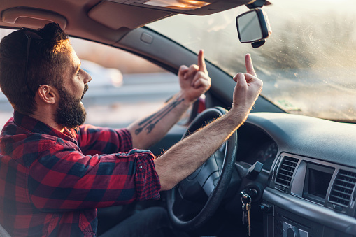 Side view image of frustrated young man shouting and making obscene gestures toward another driver