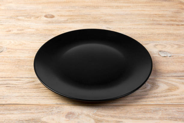 istock Perspective view. Empty black matte plate on orange wooden background 1091691268