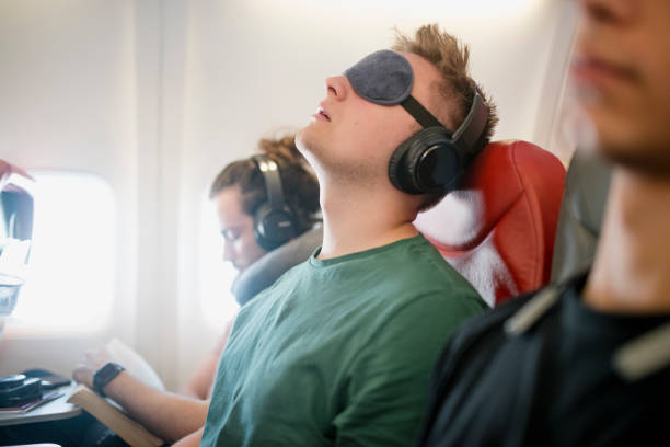 Noisy Snorer on a Flight Close up shot of a young man asleep with his head back snoring on a flight in economy class. He is wearing wireless headphones and has an eye mask on. economy class stock pictures, royalty-free photos & images