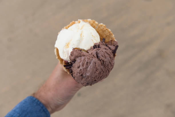 POV of a hand holding a large 3 scoop ice-cream cone at the beach, Newquay, Cornwall.