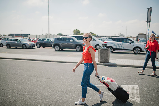 One happy young woman is crossing the airport parking lot with her baggage, looking happy to finally have arrived.