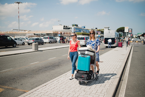 Young female couple are walking though the airport parking lot with their luggage to make their way to their hotel in Italy.