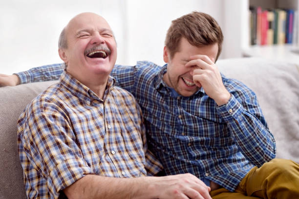 Father and son are sitting on the sofa in the living room and remember joke stock photo