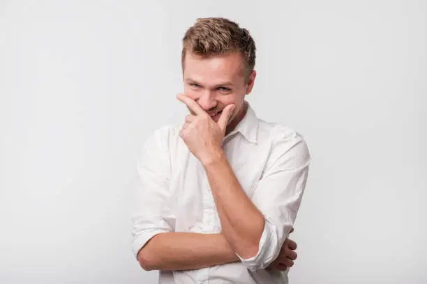 Mature man laughing and covering his mouth with hand over white background. Trying to hold a laugh not to offend some person.