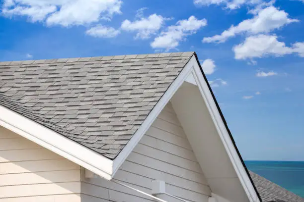 Photo of grey roof shingle with blue sky background, house roof near sea in morning time.
