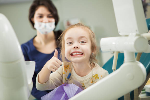 Cheerful kid with broad smile after teeth polishing procedure Cheerful kid with broad smile after painless teeth polishing procedure sits in comfortable chair at modern dentist office with mother and doctor in ask who stand behind. pediatric dentistry stock pictures, royalty-free photos & images