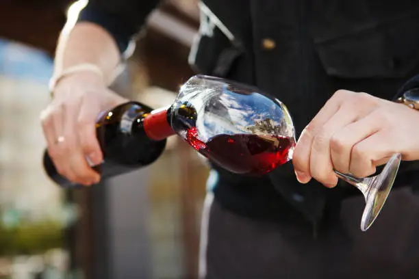 Man pouring wine into wineglass, male hand holding bottle of red expensive alcoholic beverage, closeup photo