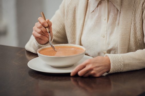 partial view of senior woman sitting at table and eating cream soup at home