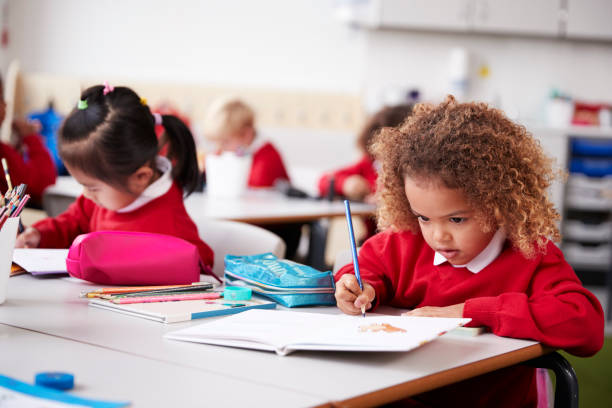 usa uniforme escolar colegiala joven sentado en un escritorio en un dibujo de aula de escuela infantil, cerca - uniforme de colegio fotografías e imágenes de stock