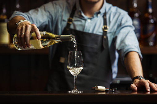 Sommelier hombre vertiendo vino blanco en copas de tallo largo. photo