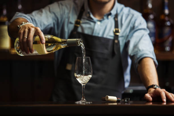 Male sommelier pouring white wine into long-stemmed wineglasses. Male sommelier pouring white wine into long-stemmed wineglasses. Waiter with bottle of alcohol beverage. Bartender at bar counter pour elite drink into long-stemmed glass pouring stock pictures, royalty-free photos & images