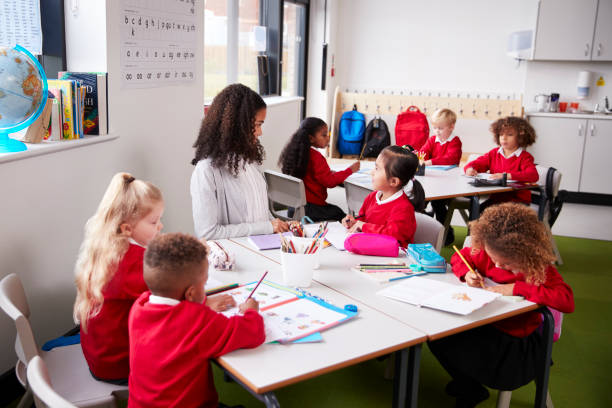 profesor de la escuela de infantil femenino joven sentado en una mesa en un salón de clases con sus alumnos - small group of people fotografías e imágenes de stock