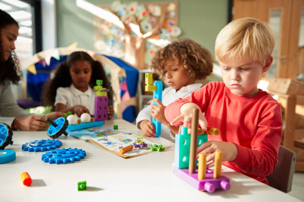 istock Infant school boy sitting at a table using educational construction toys with his classmates, close up 1091724406