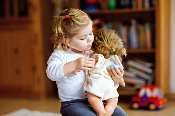 愛らしいかわいい幼児女の子人形で遊ぶ。幸せな健康な赤ちゃんの子供の役割ゲームとの楽しみを有する自宅で母親や保育園の再生します。おもちゃでアクティブな娘 - baby doll dress ストックフォトと画像