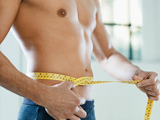 male beauty cropped view of caucasian young man measuring waist with yellow tape. Horizontal shape, mid section, side view man muscular chest stock pictures, royalty-free photos & images