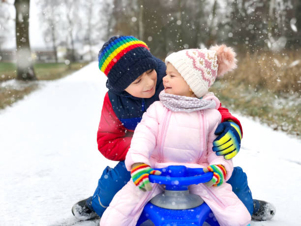 kleines kind junge und niedlichen kleinkind mädchen sitzen zusammen auf schlitten. geschwister, bruder und baby schwester schlittenfahrt bei schneefall zu genießen. kinder rodeln auf schnee. aktive unterhaltung für familienurlaub - little boys sled clothing slide stock-fotos und bilder