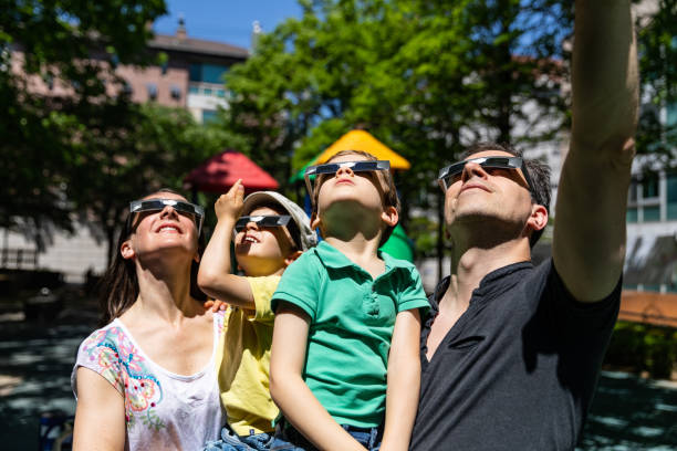 toda a família olha para o eclipse solar na rua da cidade em um parque público - eclipse - fotografias e filmes do acervo