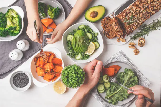 Photo of Healthy vegan food lunch, top view. Vegetarian dinner table, people eat healthy food. Salad, sweet potato, vegan cake, vegetables on white background.