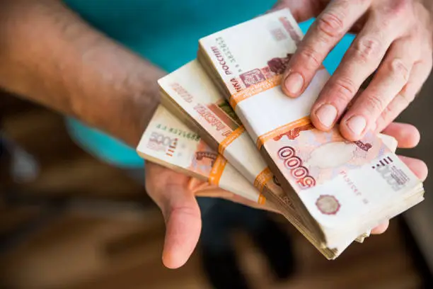 Businessman giving money, Russian Ruble banknotes, over his desk in a dark office - bribery and corruption concept