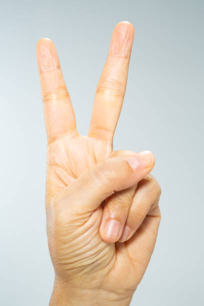istock Woman's hand raise two fingers up on grey  background, Close up & Macro shot, Selective focus, Asian body skin part, Symbol, Gesturing, Body Language concept 1091752192