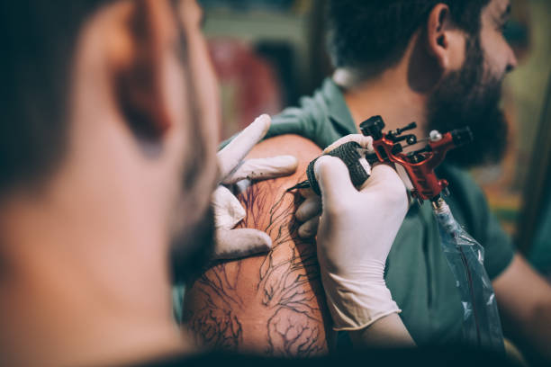 artist tattooing a man in studio - tatuagem imagens e fotografias de stock