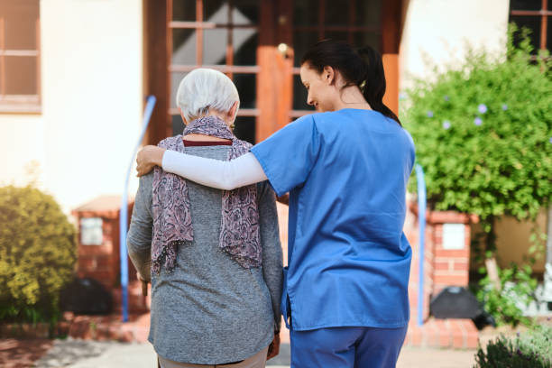 The perfect company for a stroll in the garden Rearview shot of a senior woman and a nurse going for a walk together in a retirement home garden hand on shoulder photos stock pictures, royalty-free photos & images