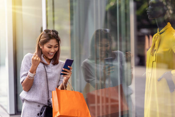 istock Asian woman cheerful when using the smart mobile phone for check online shopping order is completed with clothes beside the glassess in store shop with happy action at department center 1091767040
