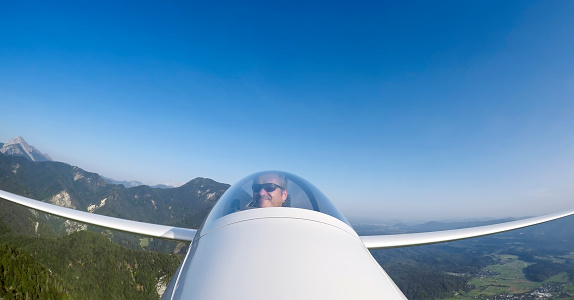 Mature man flying glider airplane against blue sky.