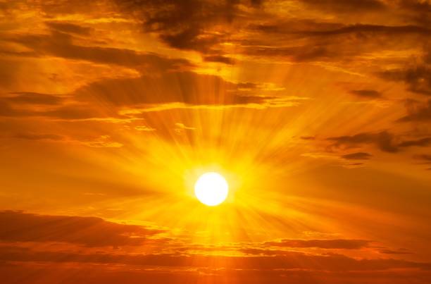 The brightly yellow sun is shining on the orange sky and clouds at golden hour time sunrise or sunset scene nature background