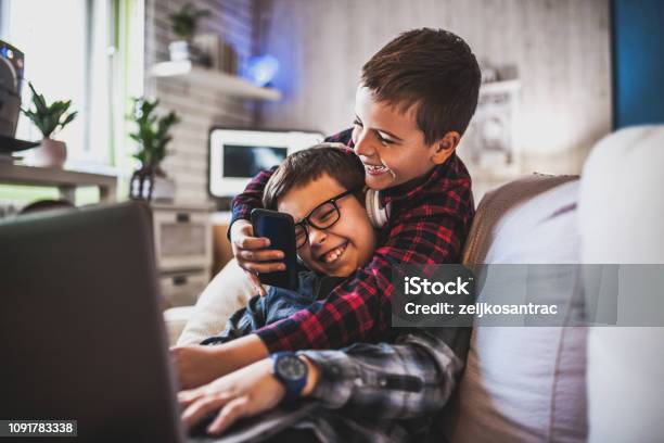 Two Teenage Boys With Gadgets On Couch At Home Stock Photo - Download Image Now - Child, Brother, Teenager