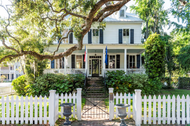 Typical American residential house building in Charleston, South Carolina area with American flag and white picket fence Mount Pleasant, USA - May 11, 2018: Typical American residential house building in Charleston, South Carolina area with American flag and white picket fence southern usa stock pictures, royalty-free photos & images