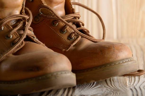 istock Yellow leather used work boots on wooden background closeup. Place for text 1091797344