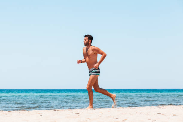 giovane bell'uomo che corre sulla spiaggia - men beach running shirtless foto e immagini stock