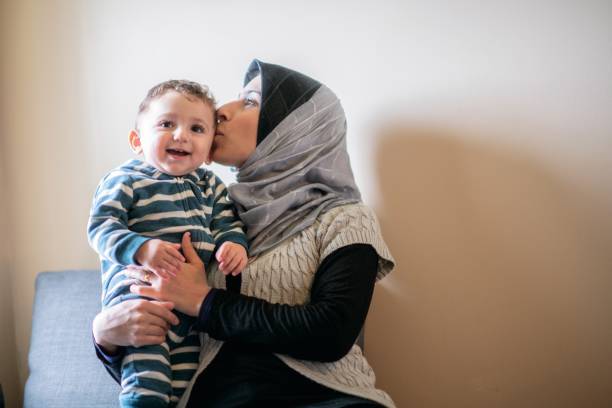 Smiling boy with mom kissing him An adorable little muslim family spends time together one afternoon in their lovely home. The mother is kissing their son. 6 11 months stock pictures, royalty-free photos & images