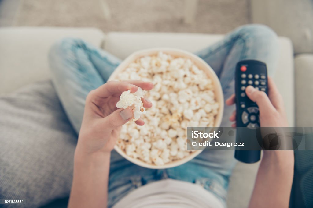High angle above top view close up cropped pow overhead first person photo of spectator lady with her brunette hair box of corn she sit in comfort modern light house hold snack and remote control Time Stock Photo