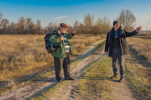 istock Two senior hikers with backpacks discussing correct path while walking on a country road 1091828176