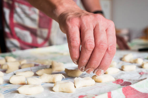 close up of italian grandma hands making fresh traditional  homemade italian gnocchi pasta on table with flour stock photo